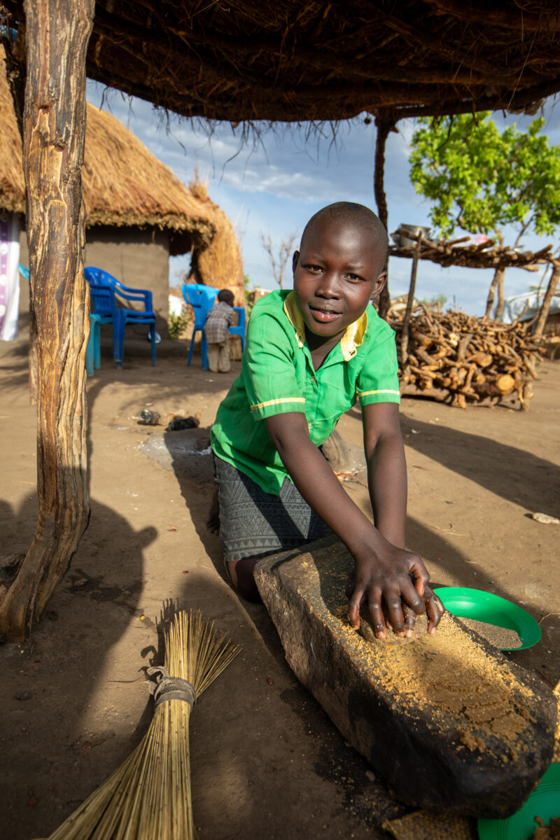 Grinding the Meal — Refugee girl grinds grain on a grinding stone. — Child, Eyes Open, Frontal Face, Male, One Face