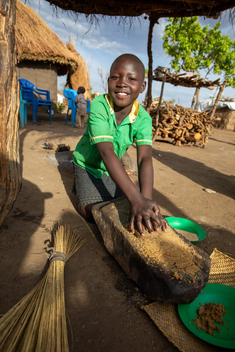 Grinding the Meal — Refugee girl grinds grain on a grinding stone. — Child, Eyes Open, Frontal Face, Male, One Face