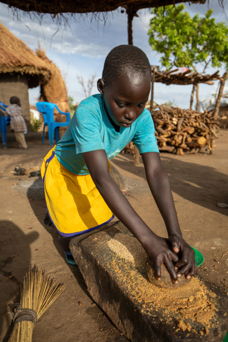 Grinding the Meal — Refugee girl grinds grain on a grinding stone. — Child, Eyes Closed, Female, Frontal Face, One Face