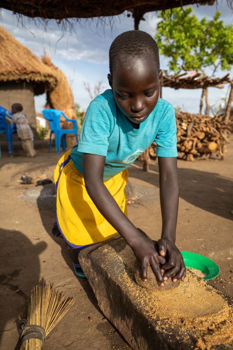 Grinding the Meal — Refugee girl grinds grain on a grinding stone. — Eyes Closed, Female, Frontal Face, One Face, Person