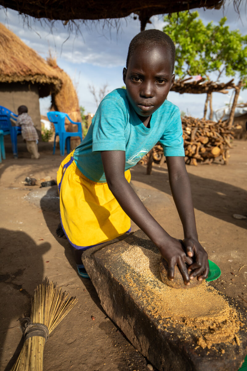 Grinding the Meal — Refugee girl grinds grain on a grinding stone. — Child, Eyes Open, Female, Frontal Face, One Face