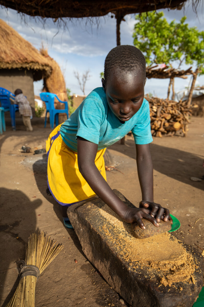 Grinding the Meal — Refugee girl grinds grain on a grinding stone. — Child, Eyes Closed, Frontal Face, One Face, Person