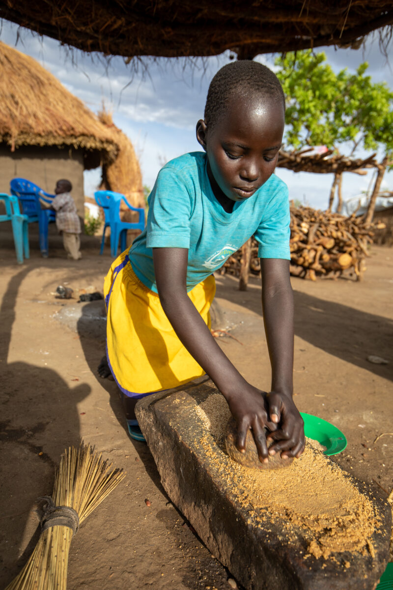 Grinding the Meal — Refugee girl grinds grain on a grinding stone. — Child, Eyes Closed, Female, Frontal Face, One Face