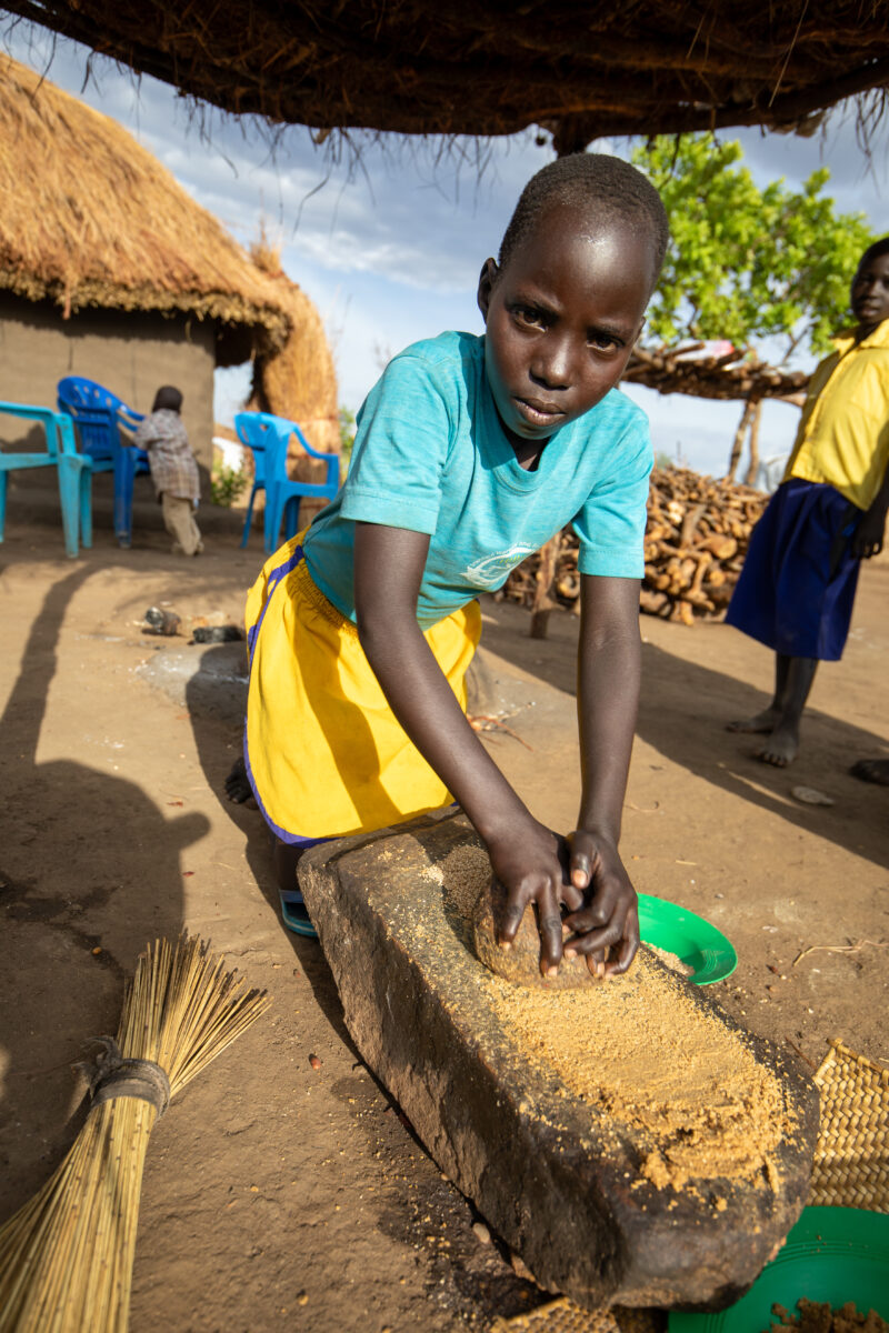 Grinding the Meal — Refugee girl grinds grain on a grinding stone. — Child, Eyes Open, Frontal Face, Male, One Face