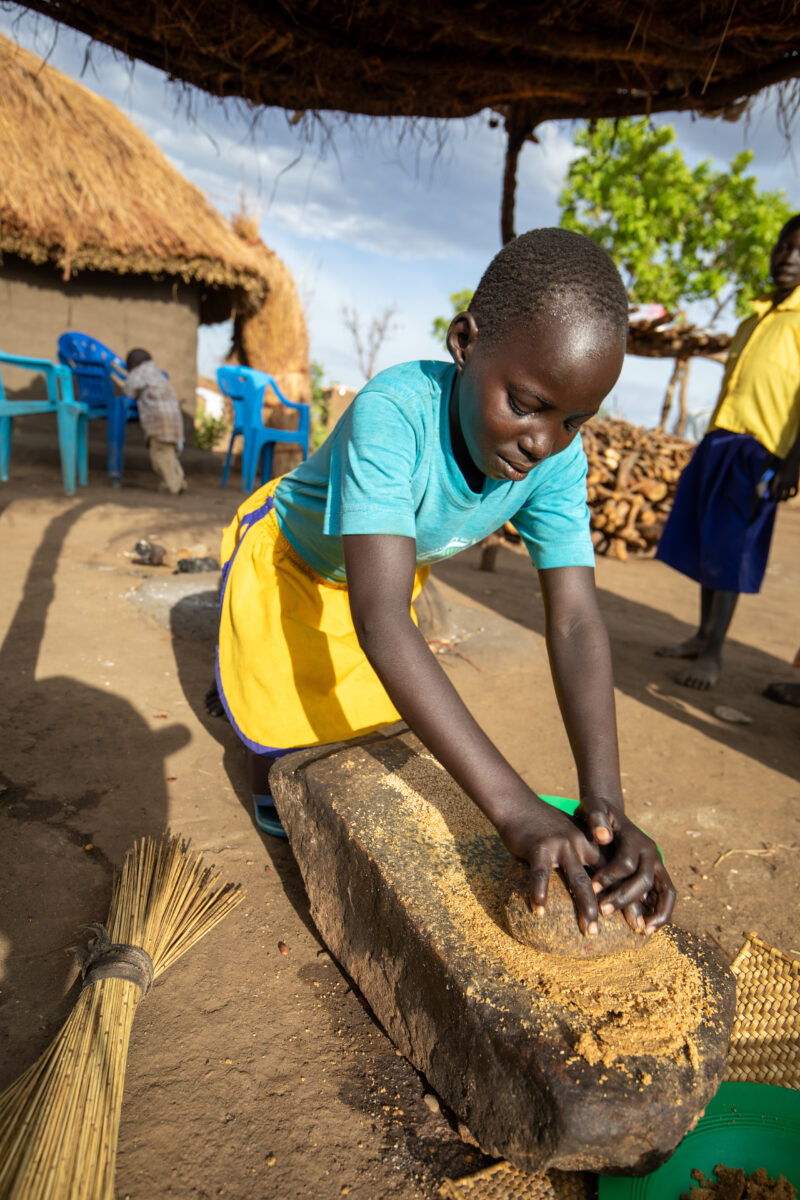 Grinding the Meal — Refugee girl grinds grain on a grinding stone. — Baby, Eyes Closed, Frontal Face, One Face, Person