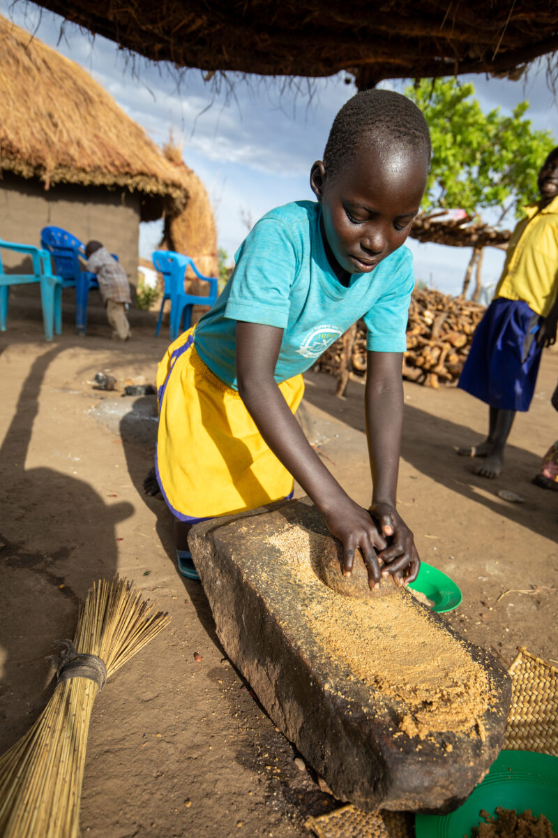 Grinding the Meal — Refugee girl grinds grain on a grinding stone. — Child, Eyes Closed, Frontal Face, Male, One Face