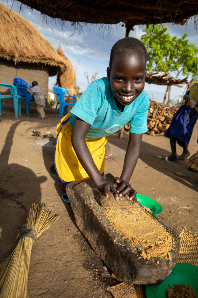 Grinding the Meal — Refugee girl grinds grain on a grinding stone. — Child, Eyes Open, Female, Frontal Face, One Face