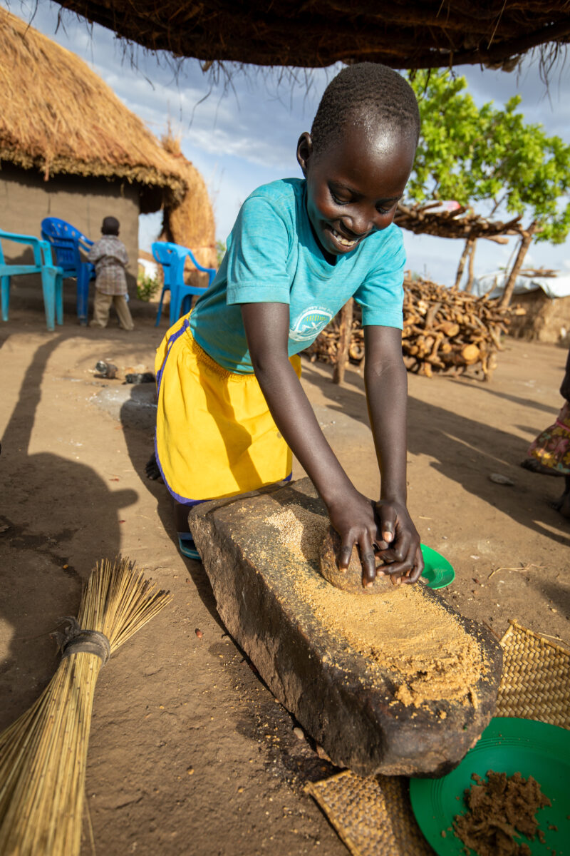 Grinding the Meal — Refugee girl grinds grain on a grinding stone. — One Face, Person, Portrait, Profile Face, Refugee