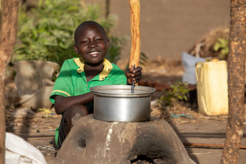 Cooking the Meal — Young refugee girl cooks a meal outdoors on a mud based cooking stove. — Child, Eyes Open, Frontal Face, Male, One Face