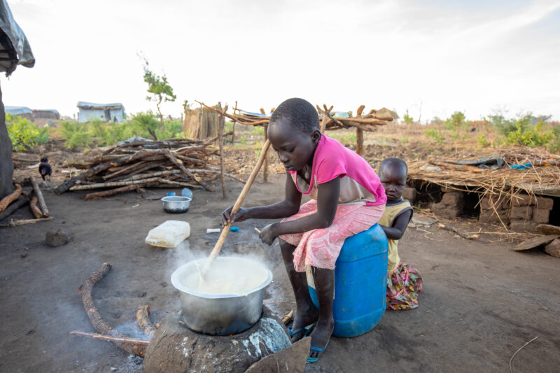 Cooking the Meal — Young refugee girl cooks a meal outdoors on a mud based cooking stove. — Child, Eyes Open, Frontal Face, Male, Person
