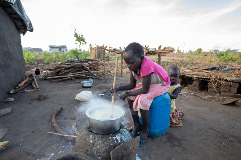 Cooking the Meal — Young refugee girl cooks a meal outdoors on a mud based cooking stove. — Child, Eyes Open, Frontal Face, Person, Profile Face