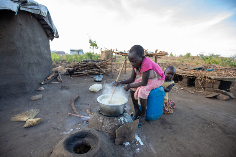 Cooking the Meal — Young refugee girl cooks a meal outdoors on a mud based cooking stove. — Child, Eyes Open, Frontal Face, Person, Profile Face