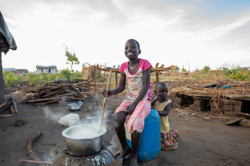 Cooking the Meal — Young refugee girl cooks a meal outdoors on a mud based cooking stove. — Eyes Open, Female, Frontal Face, One Face, Person