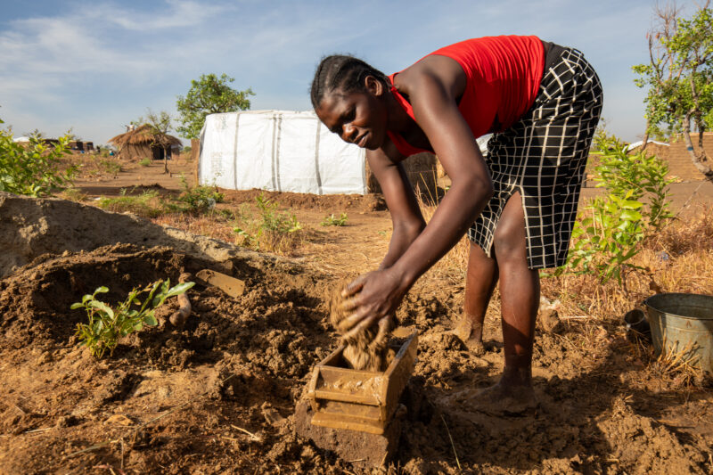 Making Bricks — South Sudan refugee woman makes mud bricks for the house that she is building at the refugee setllement. — Adult, Agriculture, Eyes Closed, F...