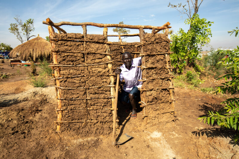 Making a Latrine — Refugee man makes a latrine by his new home in a refugee Settlement in Uganda — Adult, Complementary Colors, Eyes Open, Frontal Face, Male