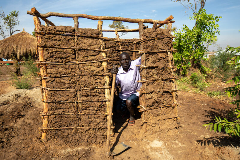 Making a Latrine — Refugee man makes a latrine by his new home in a refugee Settlement in Uganda — Adult, Eyes Open, Frontal Face, Male, One Face