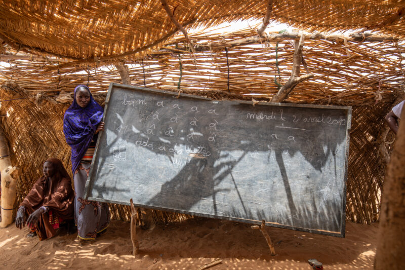 Temporary Classroom — Students in Niger, Africa, attend school in a classroom made of mud and sticks. — Adult, Africa, Boat, Education, Eyes Open