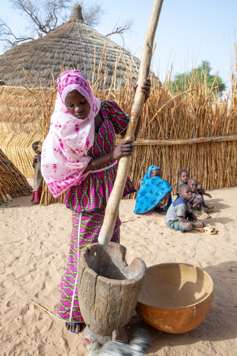 Pounding the Meal — Girl pounds sorgum into powder with a pounding stick — Africa, Child, Education, Eyes Closed, Female