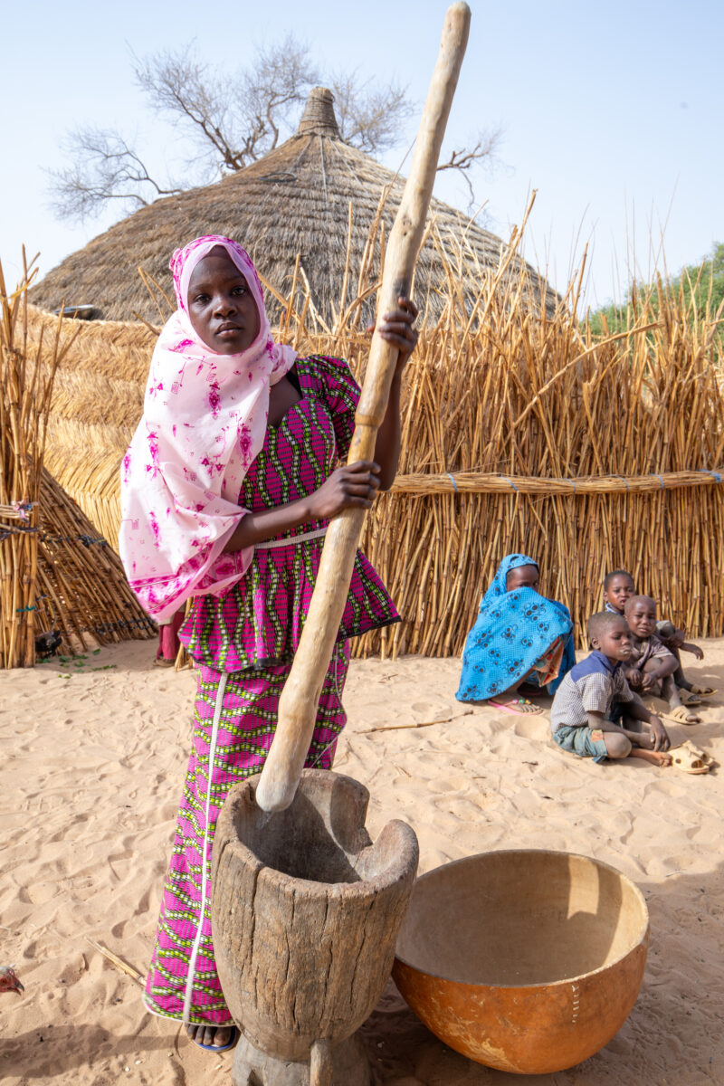 Pounding the Meal — Girl pounds sorgum into powder with a pounding stick — Africa, Baby, Child, Education, Eyes Closed