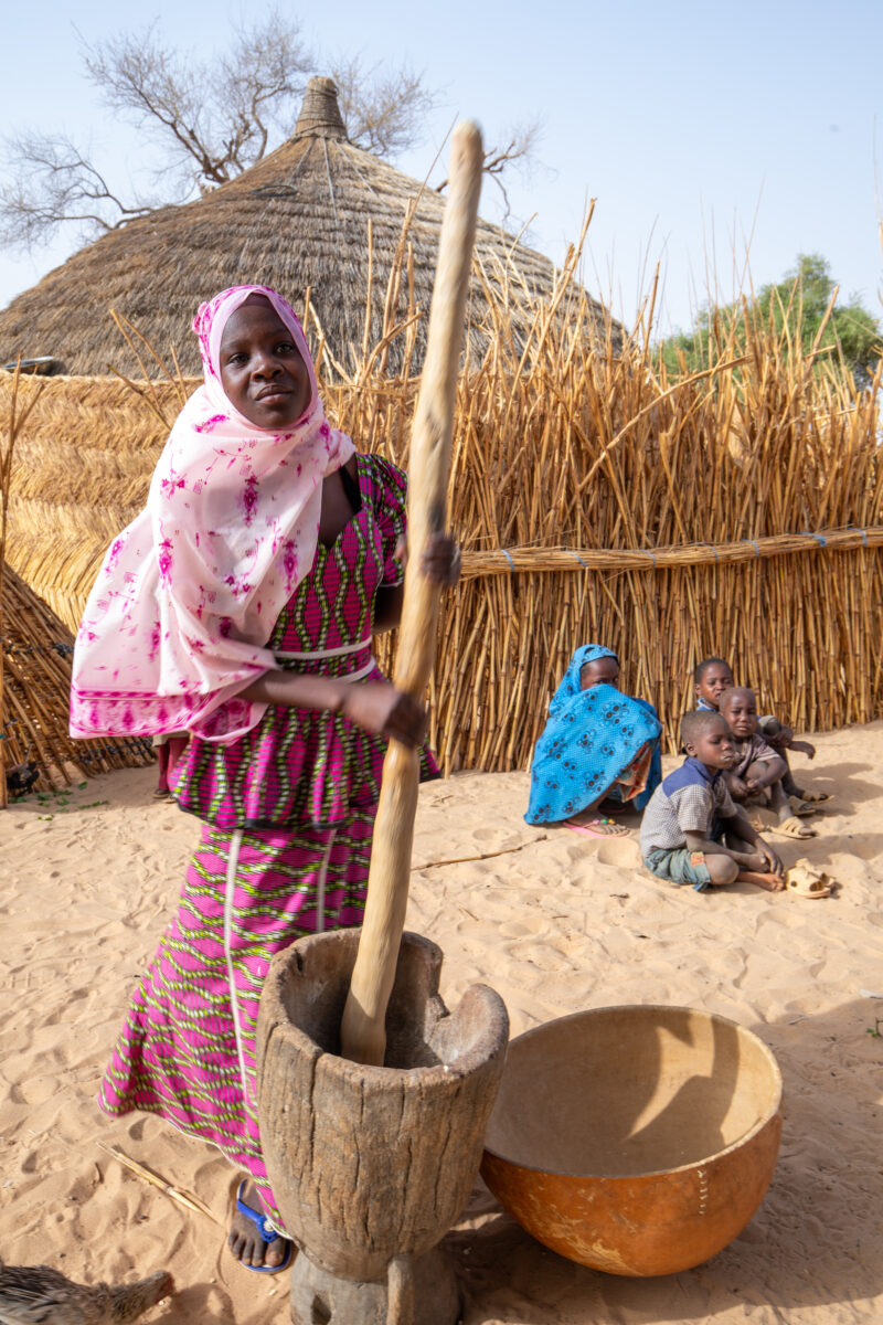 Pounding the Meal — Girl pounds sorgum into powder with a pounding stick — Africa, Child, Education, Eyes Closed, Eyes Open