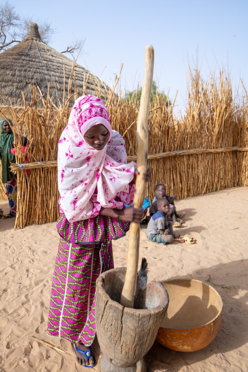 Pounding the Meal — Girl pounds sorgum into powder with a pounding stick — Adult, Africa, Child, Education, Eyes Closed