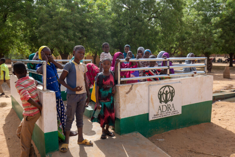 ADRA Well — Students get a refreshing drink at a well at their school provided by ADRA — Adult, Africa, Boat, Child, Education