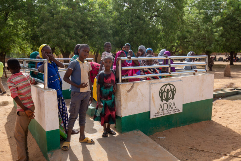 ADRA Well — Students get a refreshing drink at a well at their school provided by ADRA — Adult, Africa, Boat, Canoe, Child