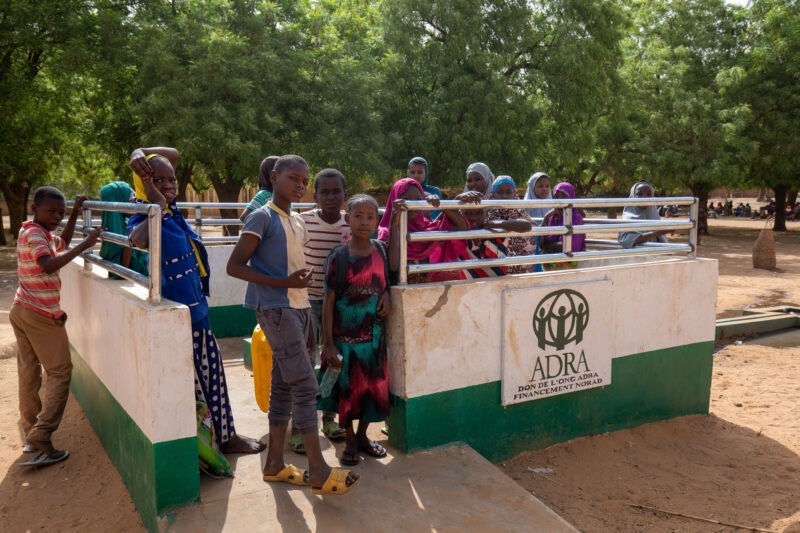 ADRA Well — Students get a refreshing drink at a well at their school provided by ADRA — Adult, Africa, Boat, Canoe, Child