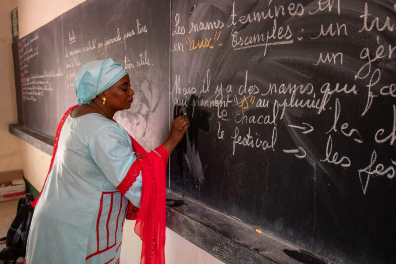 Teacher at Blackboard — Teacher writes out lesson on a blackboard at a school in Niger, Africa. — Africa, Education, Niger, One Face, Person