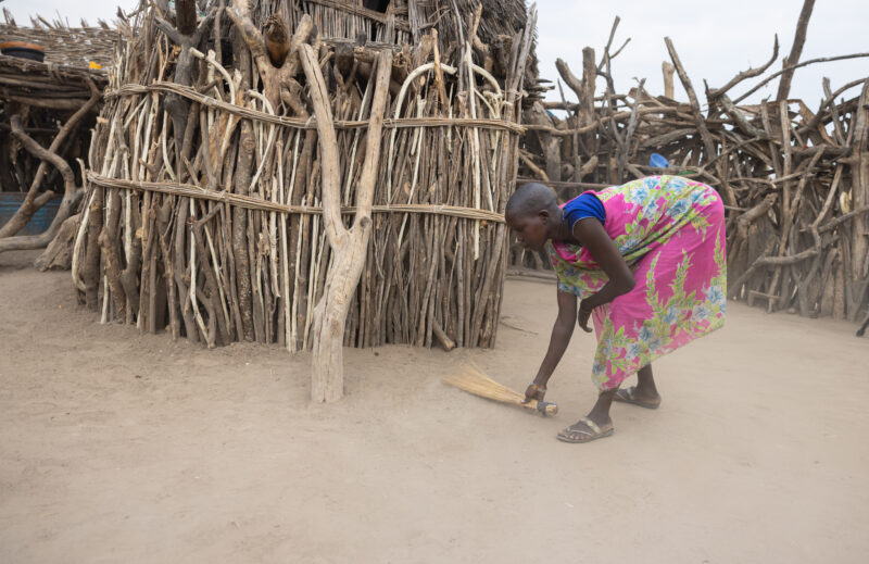 Sweeping the Compound — Girl in South Sudan sweeps the compound of her family as a morning chore every day. — Person, South Sudan, Africa, Pastoralists, Ethnic