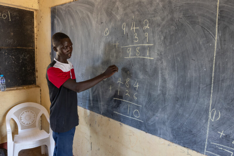 Math Teacher in South Sudan — Young teacher at a rural school in Africa teaches math. — Adult, Beard, Frontal Face, Male, One Face