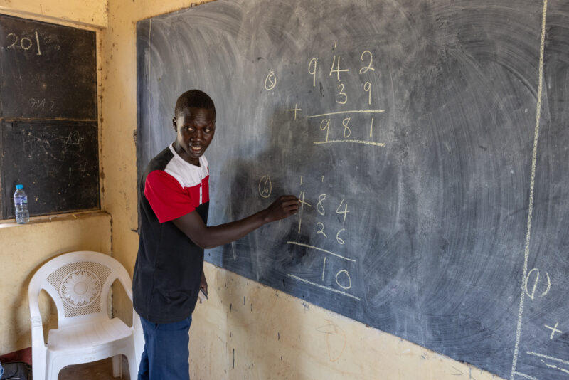 Math Teacher in South Sudan — Young teacher at a rural school in Africa teaches math. — Adult, Eyes Closed, Frontal Face, Male, One Face