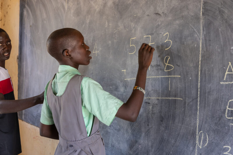 Doing Math on the Board — Young girl in South Sudan does a math problem on the blackboard of her school. — One Face, Person, Profile Face, Seminar Room, Sout...
