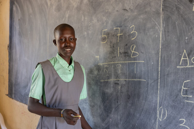 Doing Math on the Board — Young girl in South Sudan does a math problem on the blackboard of her school. — Adult, Eyes Open, Frontal Face, Male, One Face