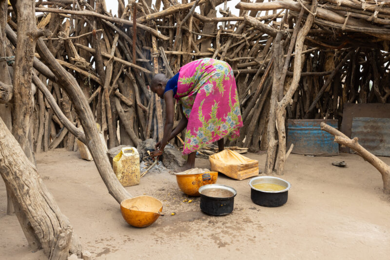 Cooking Breakfast in Rural Africa — Young girl cooks sorghum breakfast over an open fire in the compound of her home. — Person, South Sudan, Africa, Pastoral...