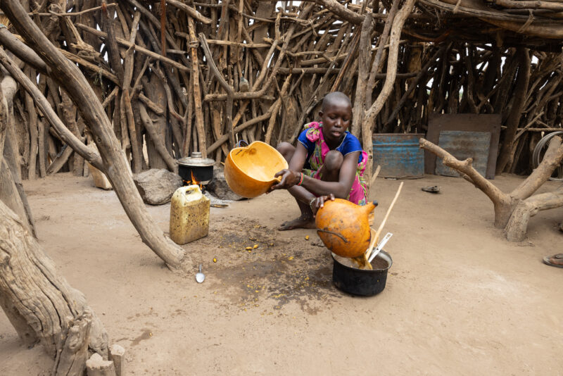 Cooking Breakfast in Rural Africa — Young girl cooks sorghum breakfast over an open fire in the compound of her home. — Frontal Face, One Face, Person, South...