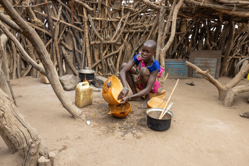 Cooking Breakfast in Rural Africa — Young girl cooks sorghum breakfast over an open fire in the compound of her home. — Drums, Frontal Face, Musical Instrume...