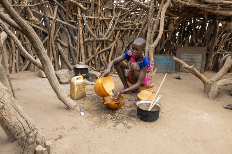 Cooking Breakfast in Rural Africa — Young girl cooks sorghum breakfast over an open fire in the compound of her home. — Drums, Frontal Face, Musical Instrume...