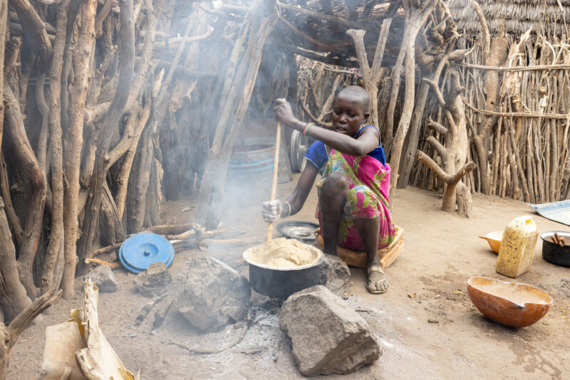 Cooking Breakfast in Rural Africa — Young girl cooks sorghum breakfast over an open fire in the compound of her home. — Frontal Face, One Face, Person, South...