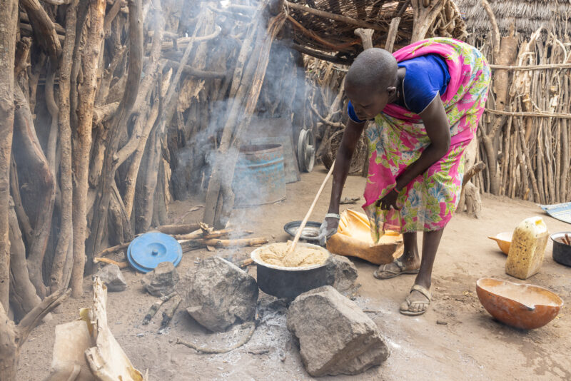 Cooking Breakfast in Rural Africa — Young girl cooks sorghum breakfast over an open fire in the compound of her home. — One Face, Person, Profile Face, South...