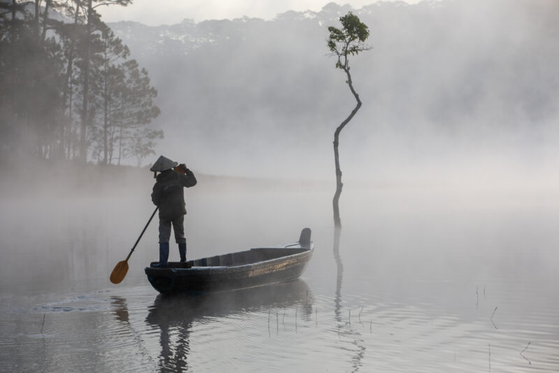 Early Morning on the Lake — Fog and mist rise up from a Lake in Vietnam making a scenic splender with a man in his fishing boat. — Colorless, Nature, Person,...