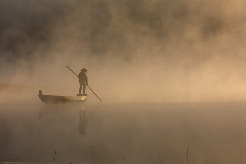 Early Morning on the Lake — Fog and mist rise up from a Lake in Vietnam making a scenic splender with a man in his fishing boat. — Colorless, Fog, Nature, Pe...