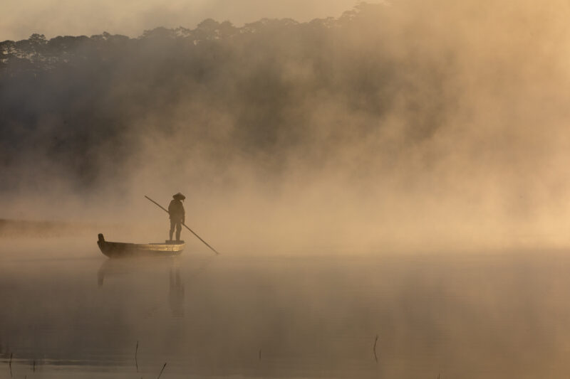 Early Morning on the Lake — Fog and mist rise up from a Lake in Vietnam making a scenic splender with a man in his fishing boat. — Colorless, Nature, Person,...