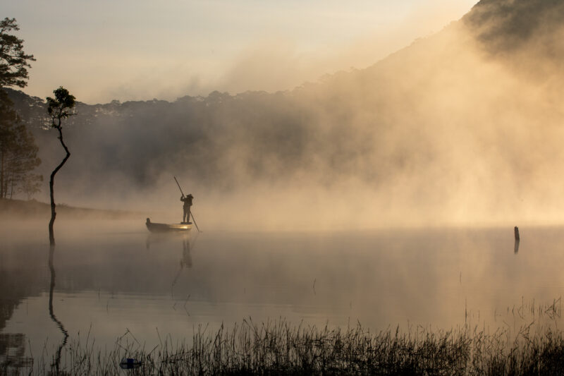 Early Morning on the Lake — Fog and mist rise up from a Lake in Vietnam making a scenic splender with a man in his fishing boat. — Colorless, Fog, Nature, Vi...
