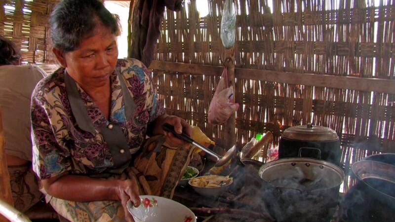 Bamboo Kitchen — Woman cooks over a fire in her kitchen inside her bamboo home.
