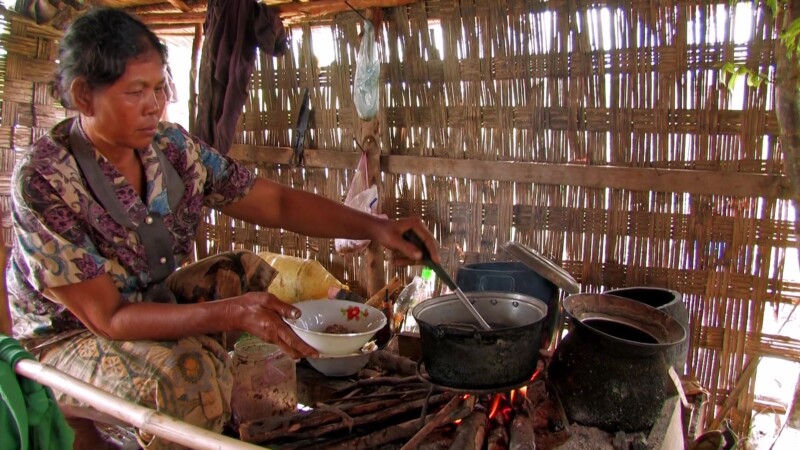 Bamboo Kitchen — Woman cooks over a fire in her kitchen inside her bamboo home.